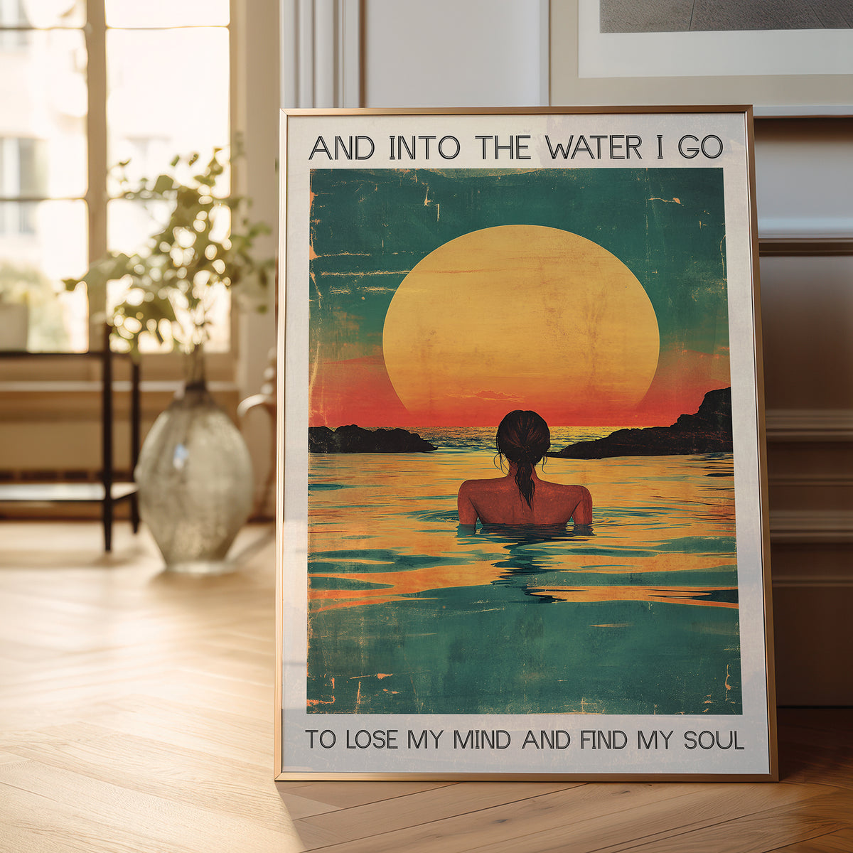 Framed poster of a woman in water with a sunset, placed on a wooden floor.