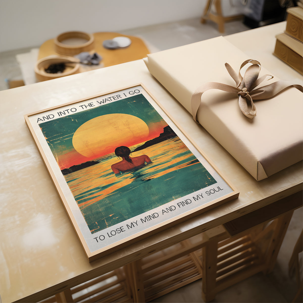 Poster with artistic design of a person in water and sunset, placed on a table with a wrapped gift.