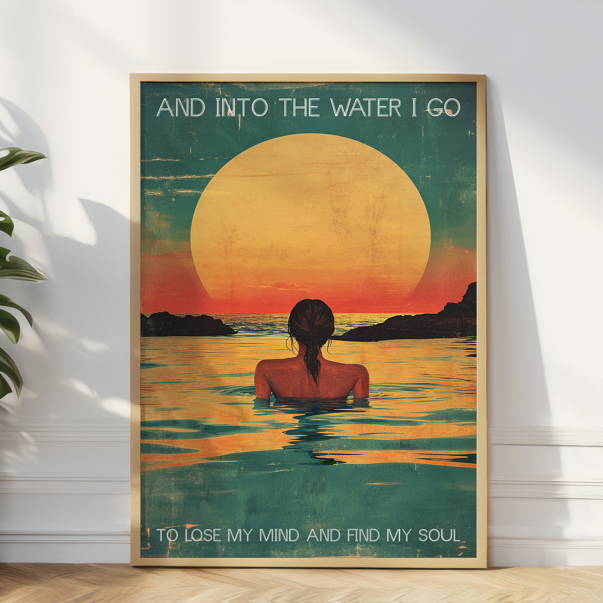 Framed artwork of a woman in water with a sunset, text 'And into the water I go / To lose my mind and find my soul' on a white wall.