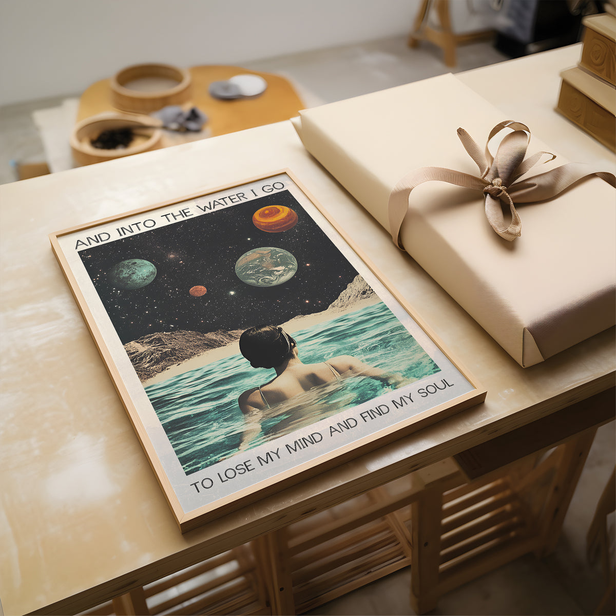 Poster of a person in water with planets and text, placed on a wooden surface next to a wrapped gift.