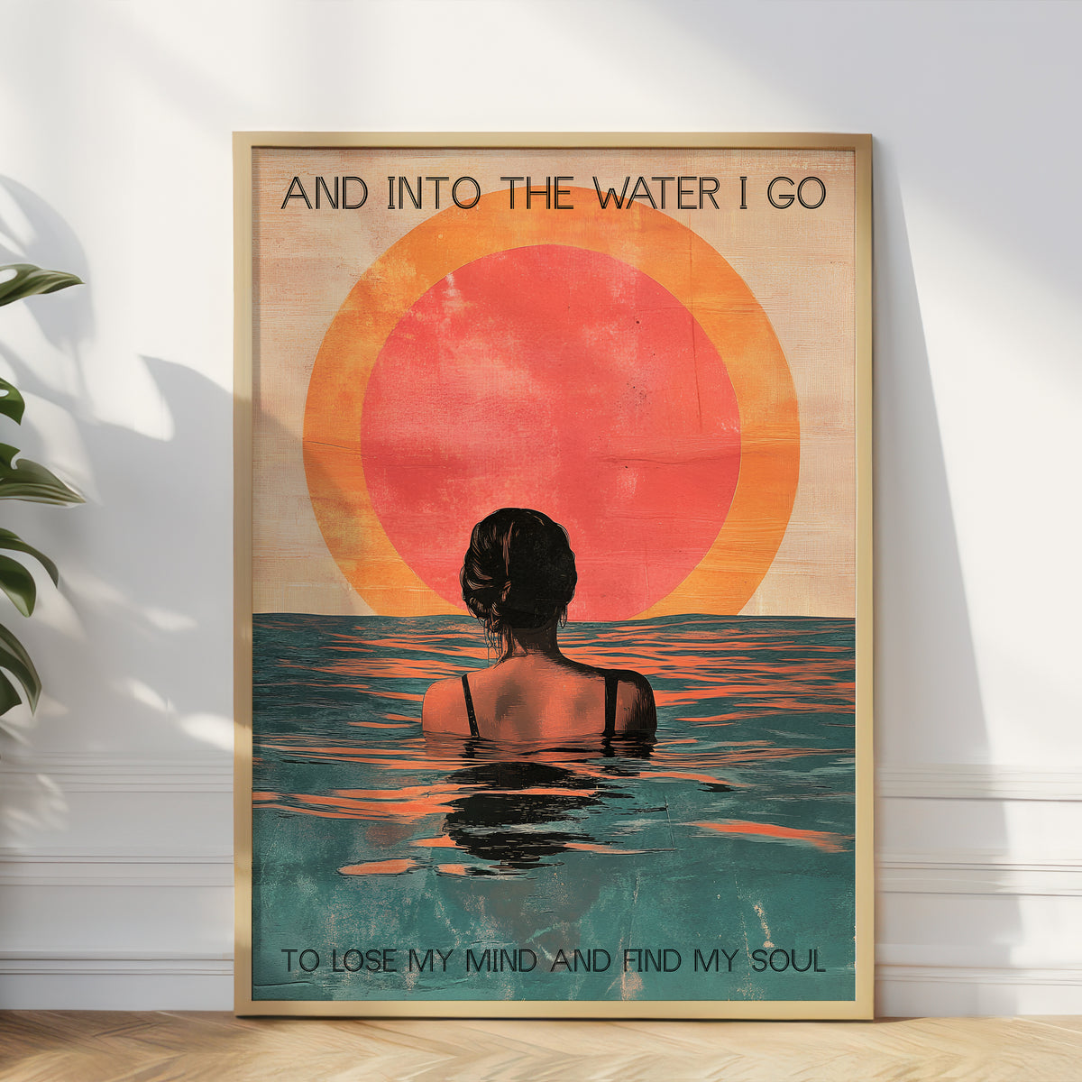 Framed artwork of a woman in water with a sunset, text 'And into the water I go / To lose my mind and find my soul' on a white wall.