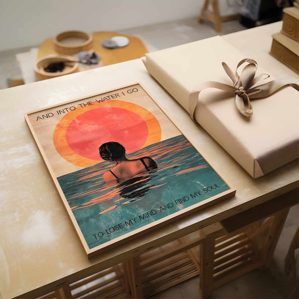 Poster of a person in water with a sunset and text, placed on a table with a wrapped gift.