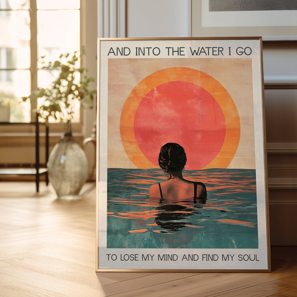 Framed poster of a woman in water with a sunset, placed on a wooden floor.