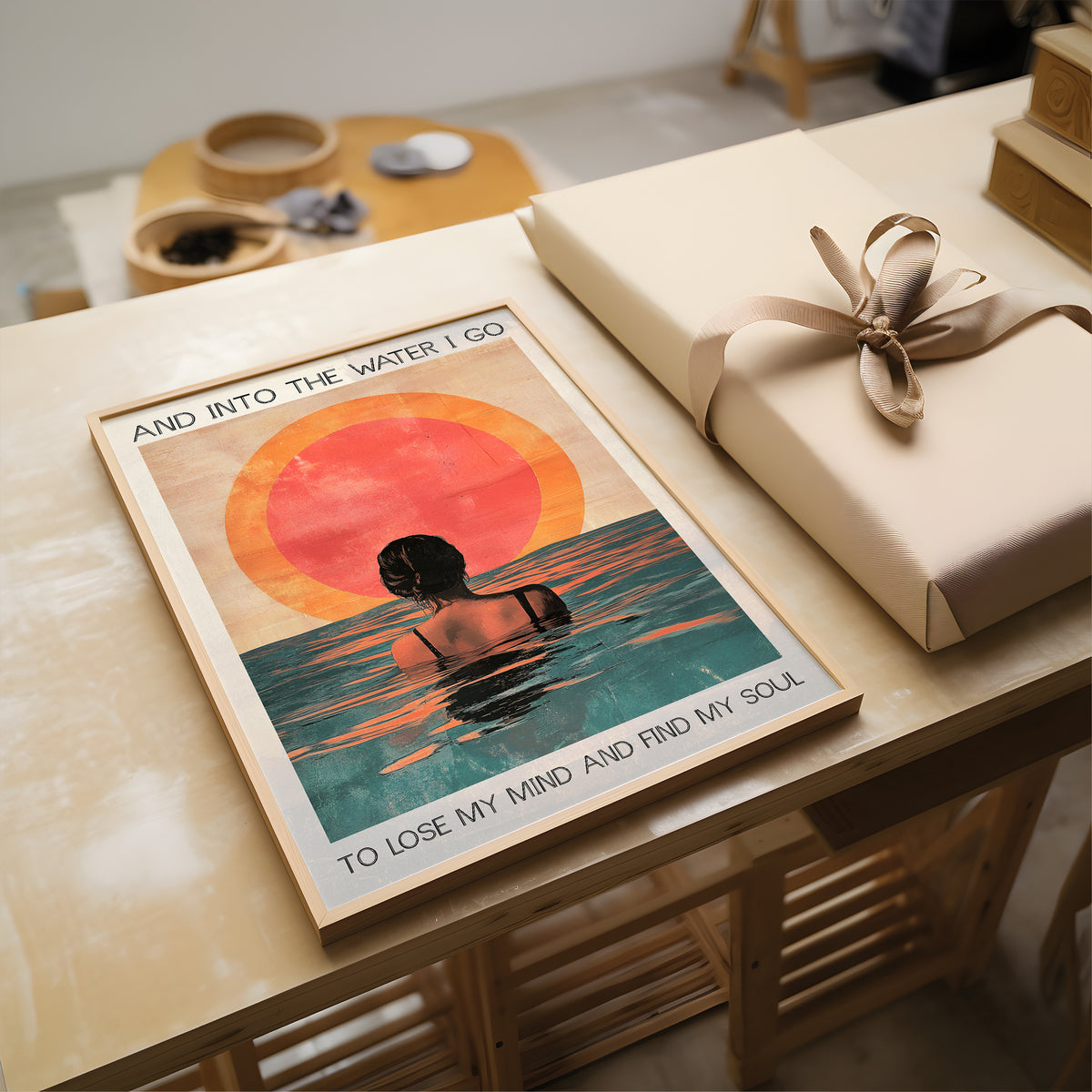 Poster with artistic design of a person in water and sunset, placed on a table with a wrapped gift.