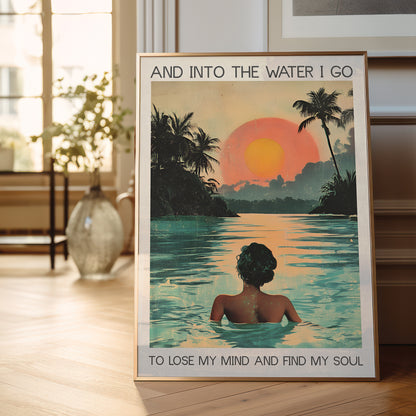 Framed poster of a woman in water with a sunset and palm trees, text 'And into the water I go / To lose my mind and find my soul' on a wooden floor.