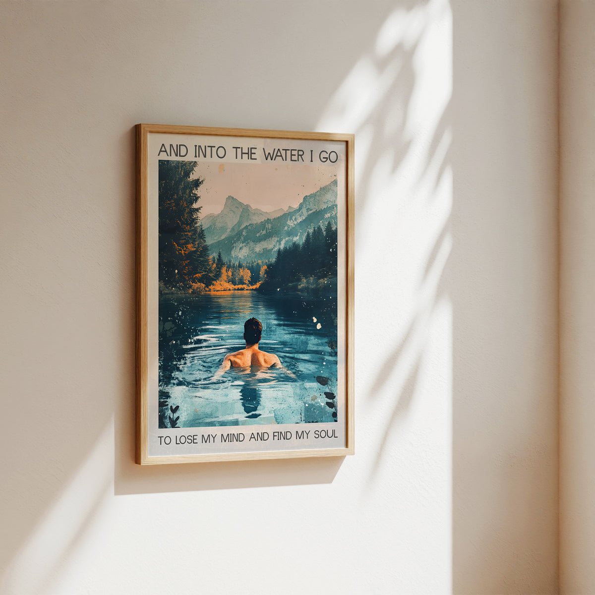 Framed poster of a person in a lake with mountains, text 'And into the water I go to lose my mind and find my soul', on a wall.