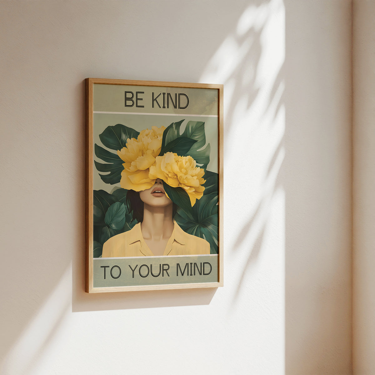 Framed artwork with a woman's face covered by yellow flowers and text 'Be kind to your mind' on a beige wall.