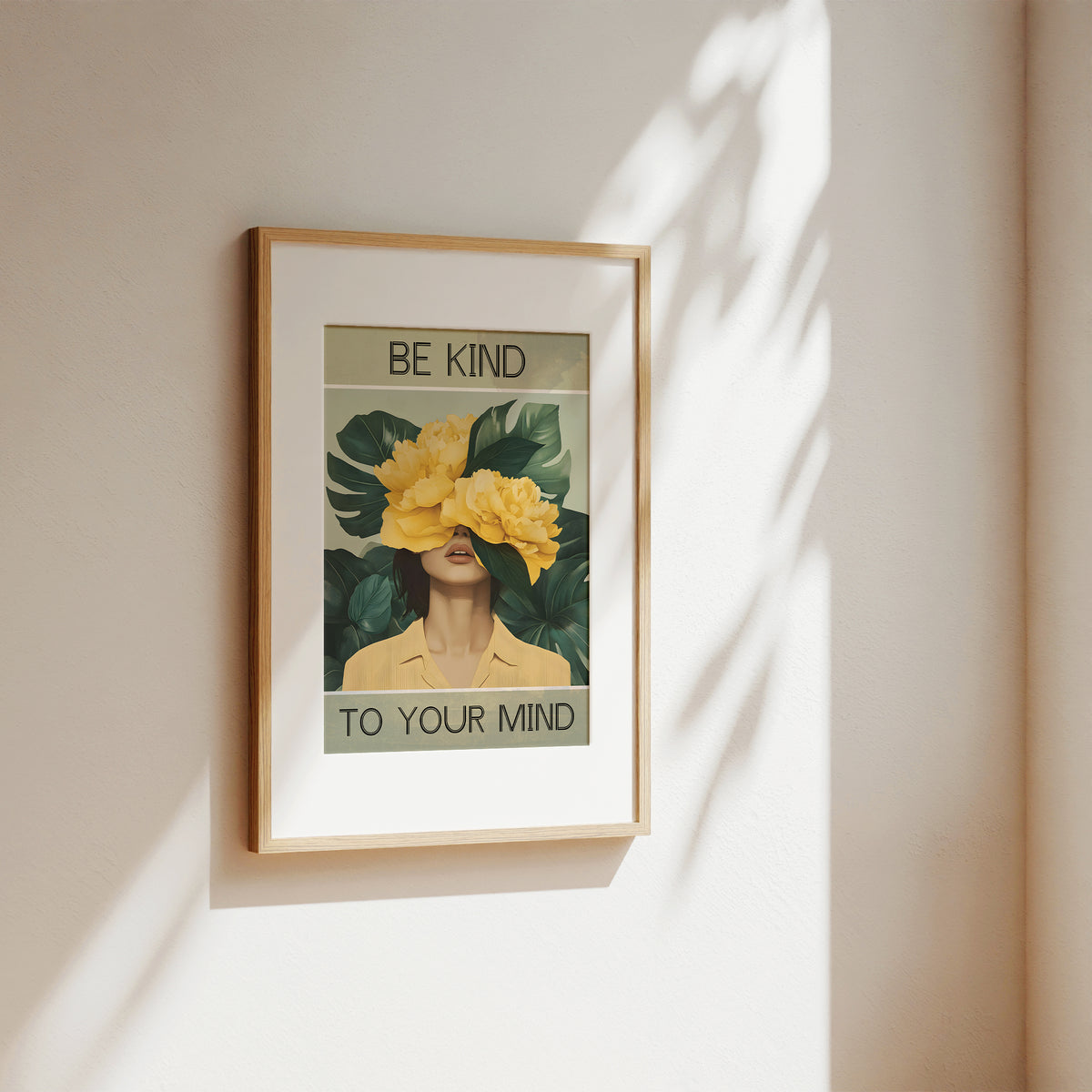 Framed artwork with a woman's face covered by flowers and 'Be Kind to Your Mind' text on a beige wall.