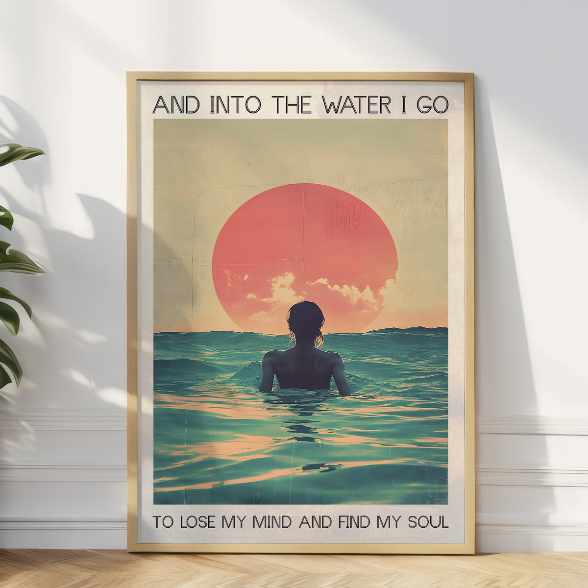 Framed poster of a person in the water with a sunset, text 'And into the water I go / To lose my mind and find my soul', on a white wall.