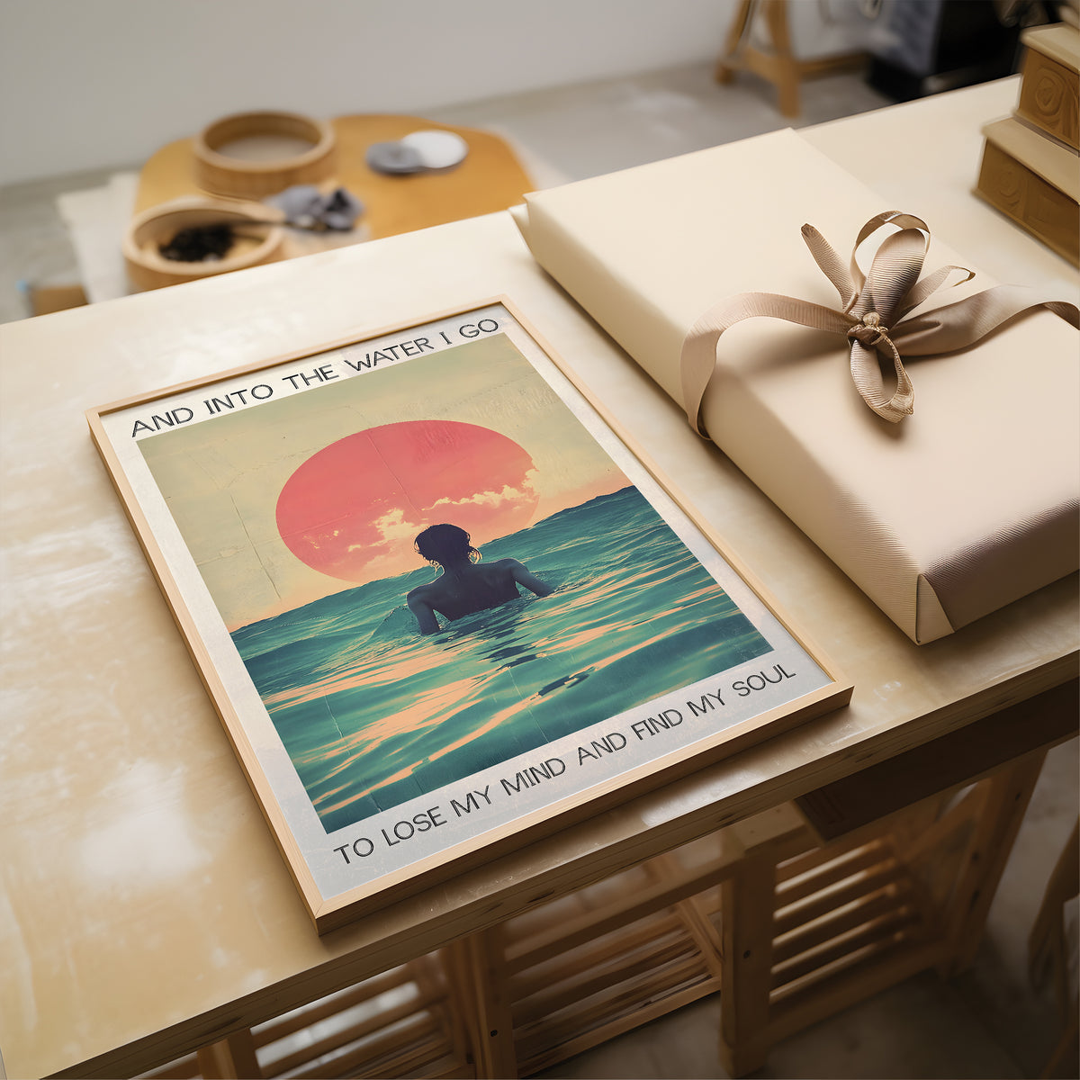 Poster of a person in water with a sunset and text, placed on a table with a wrapped gift.