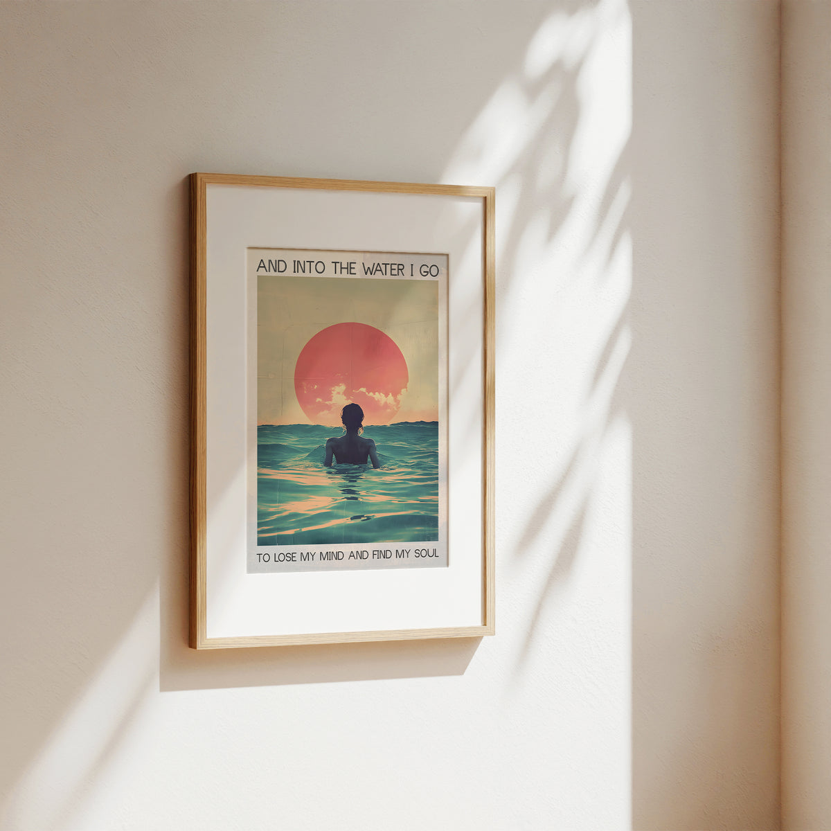Framed artwork of a person in the water with a sunset, on a beige wall.