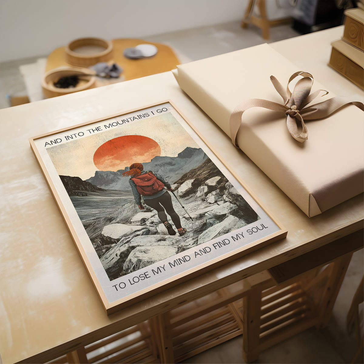 Poster of a person hiking with a mountain scene and text, placed on a wooden surface next to a wrapped gift.