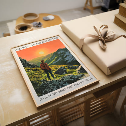 Poster of a mountain scene with a person and text, placed on a table next to a wrapped gift.