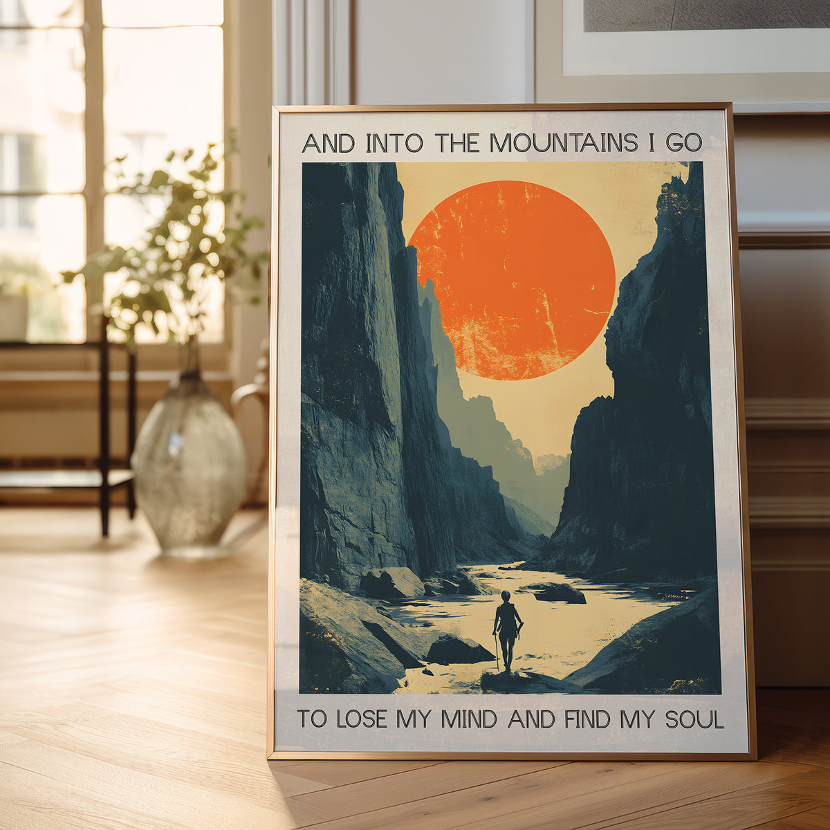 Framed poster of a mountain landscape with a person walking, featuring text 'And into the mountains I go to lose my mind and find my soul', displayed in a room.