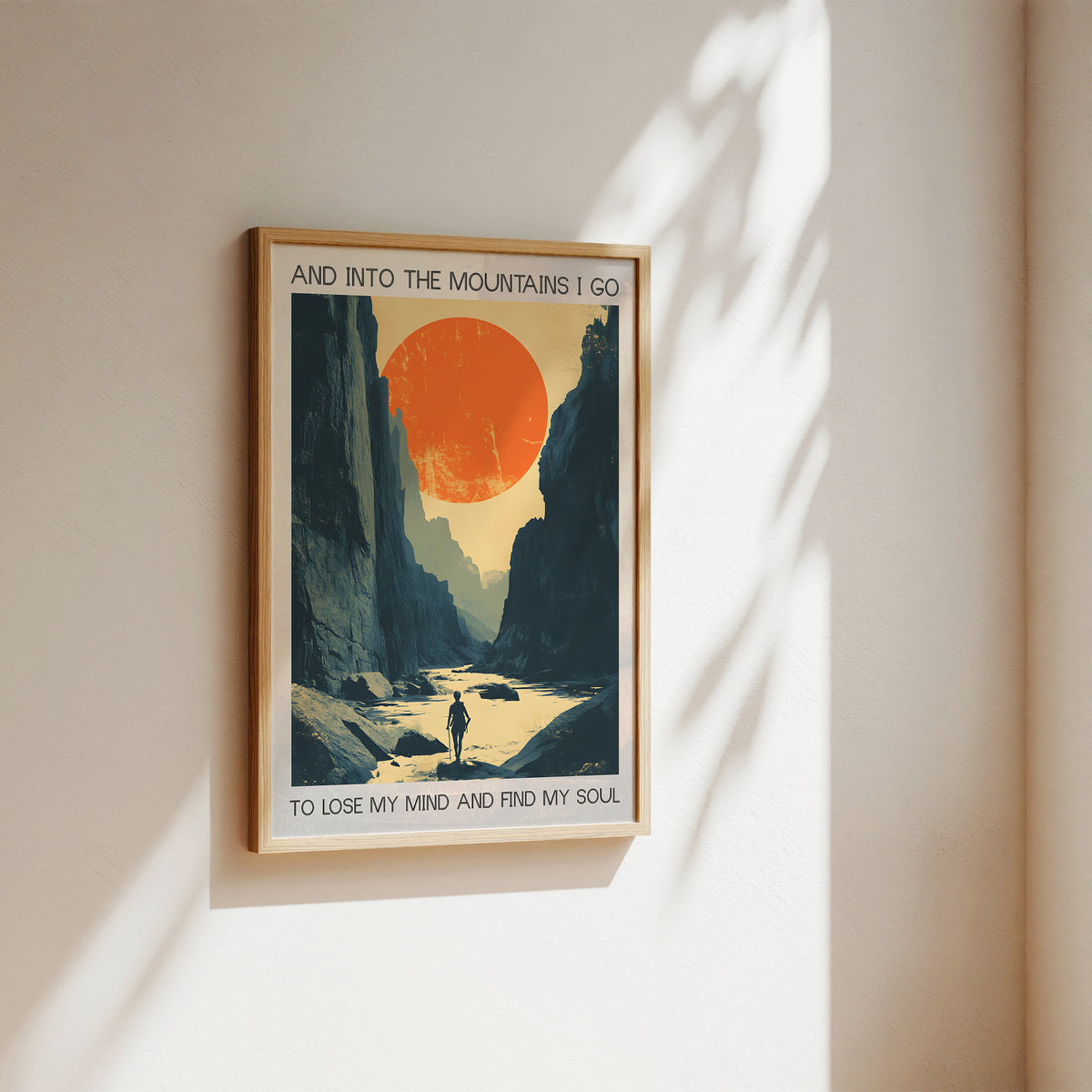 Framed poster of a mountain landscape with a person walking towards a sunset, on a beige wall.