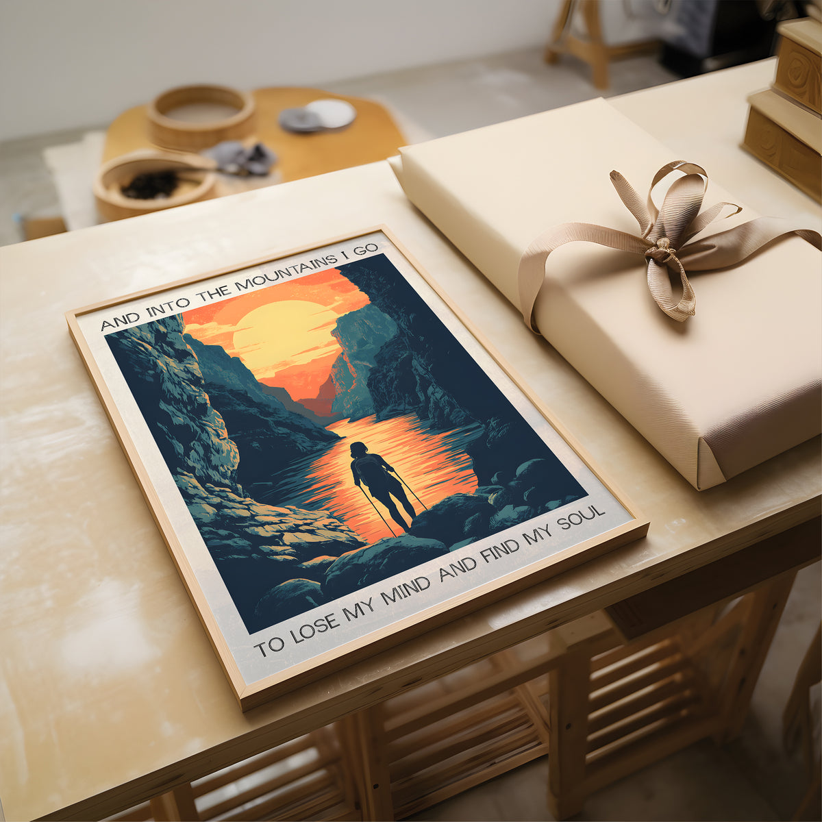 Poster of a mountain scene with a person and text, placed on a table next to a wrapped gift.