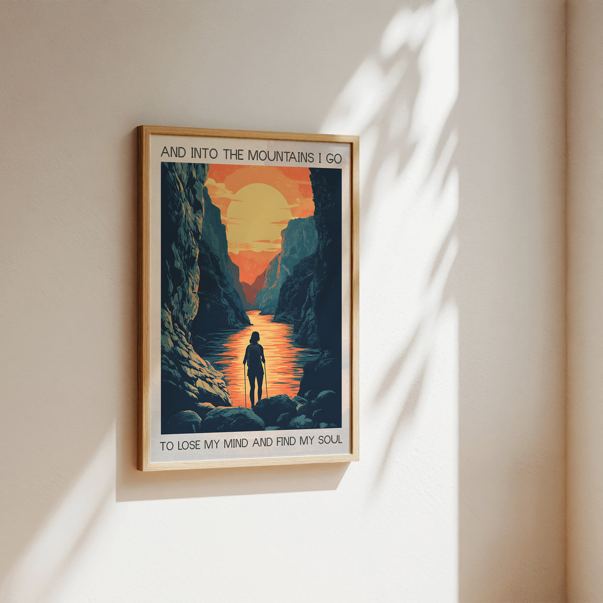Framed poster of a mountain scene with a person walking, featuring text on a beige wall.