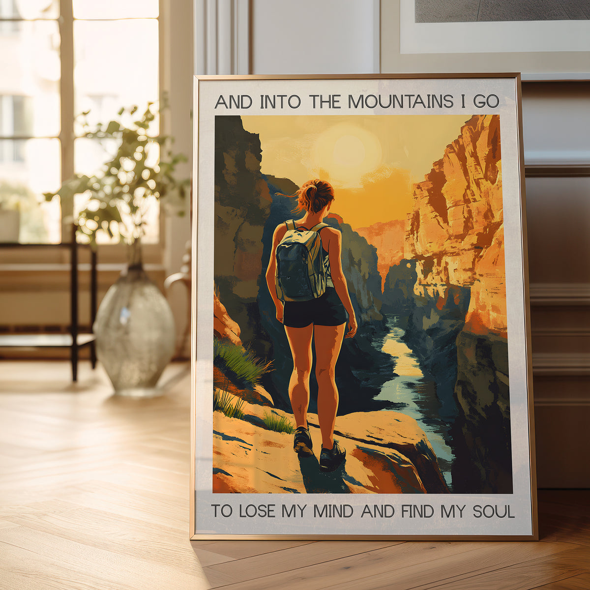 Framed poster of a woman hiking with text 'And into the mountains I go to lose my mind and find my soul' on a wooden floor.