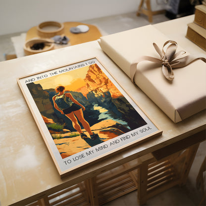 Poster of a person hiking with mountains and text, placed on a wooden surface next to a wrapped gift.