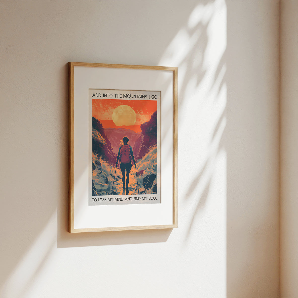 Framed poster of a mountain scene with a person walking, on a beige wall.