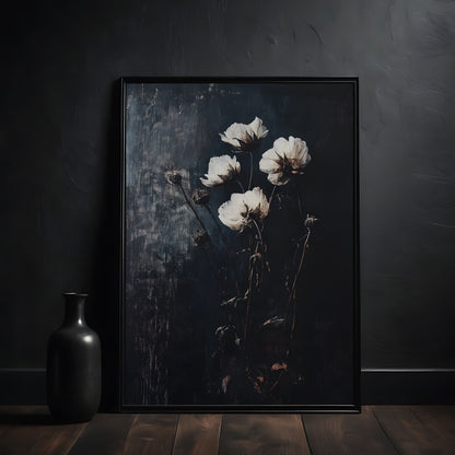 Framed artwork of white flowers on a dark background, placed on a wooden surface with a black vase beside it.