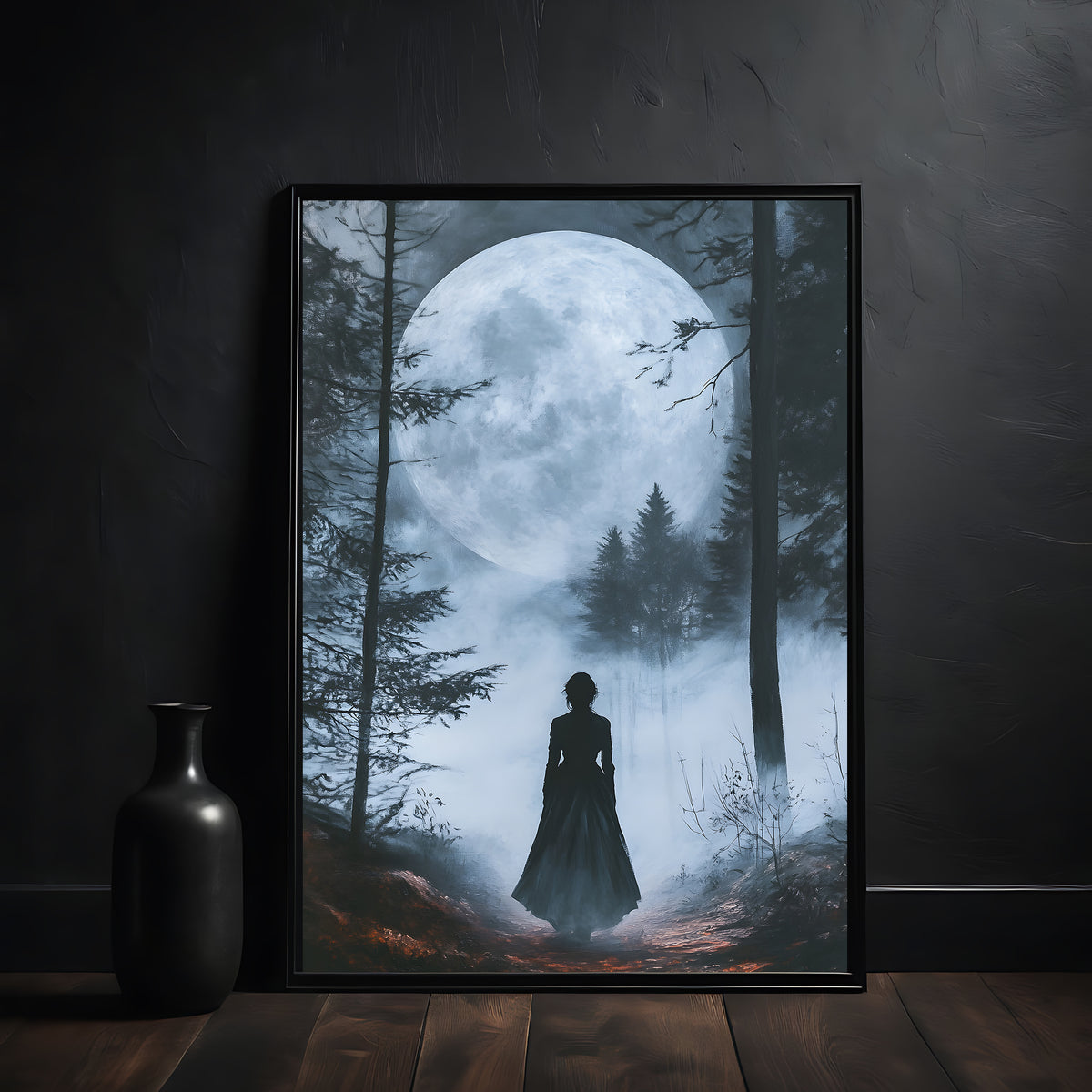 Framed artwork of a silhouette of a person in a forest with a large moon, placed on a wooden surface against a dark wall.
