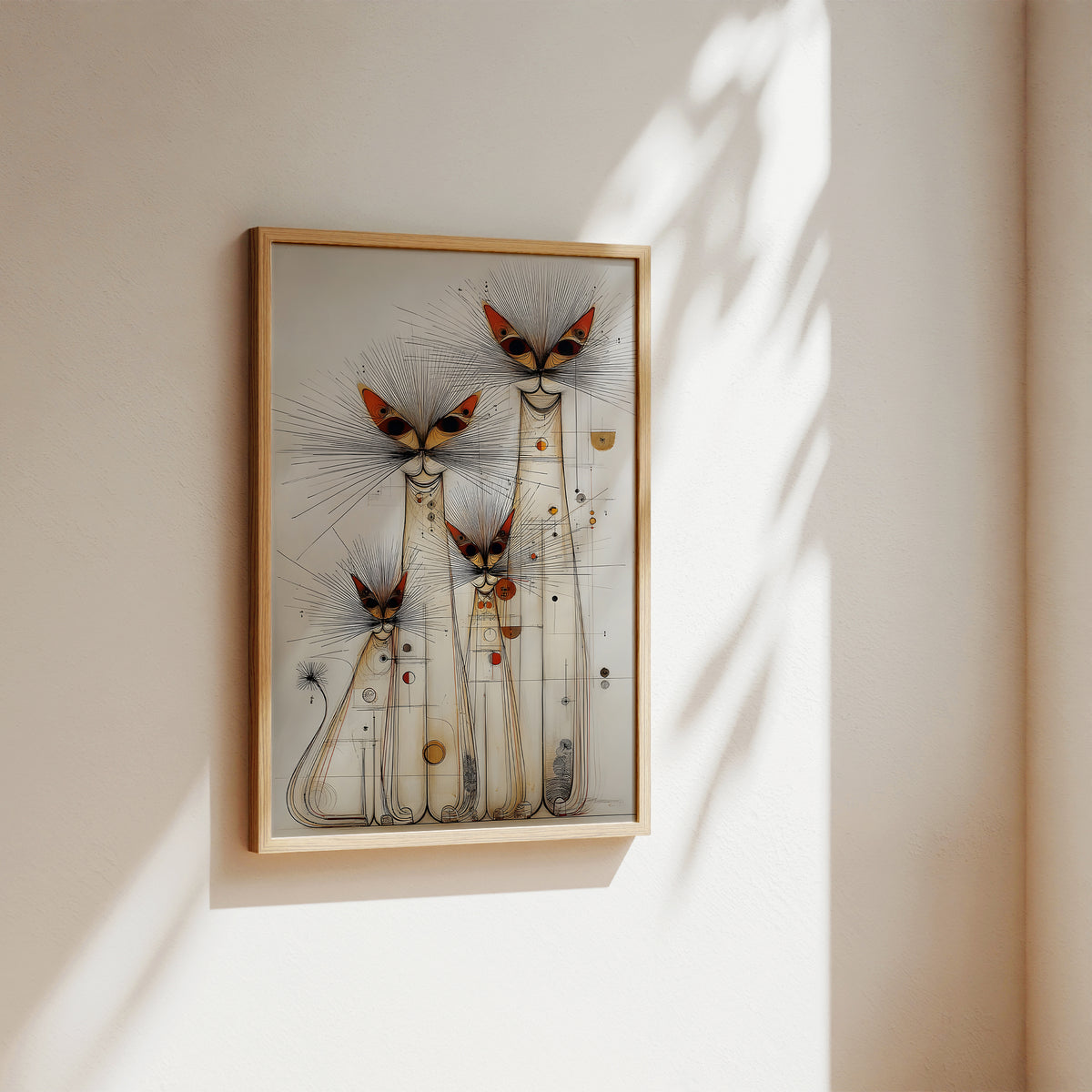 A framed abstract art print featuring three stylized cat-like figures with long radiating lines and small orange, red, and gold accents, hanging on a warm beige wall with soft sunlight and leaf shadows.